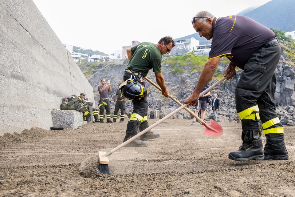 Firefighters sweep ashes covering the port town of Ginostra on July 4, 2019, a day after the Stromboli volcano erupted, killing a hiker and forcing tourists to flee. 