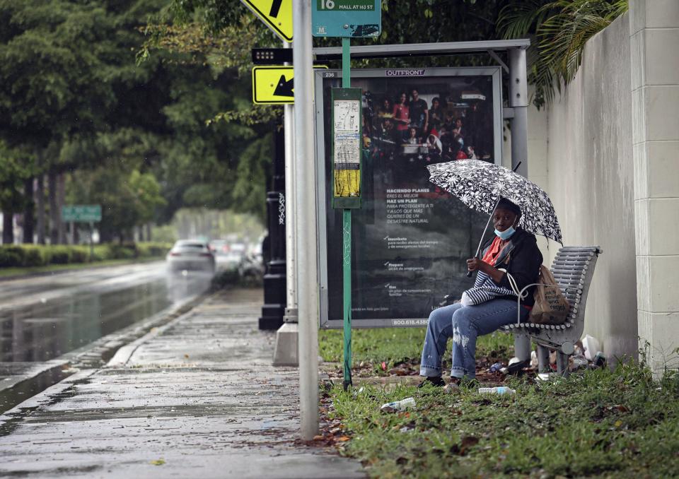 A woman sits at a bus stop on Biscayne Boulevard during a rain storm, Wednesday, April 12, 2023, in Miami. A torrential storm bought heavy showers, gusty winds and thunderstorms to South Florida on Wednesday and prompted the closure of Fort Lauderdale-Hollywood International Airport and the suspension of high-speed commuter rail service in the region.(Alie Skowronski/Miami Herald via AP)