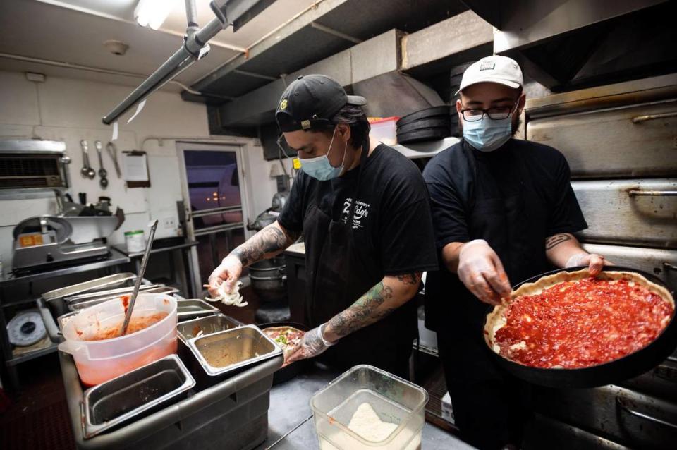 Pizza cook Christian Moreno, right, walks around another cook to add toppings to a Chicago-style deep dish pie in the small kitchen at Zelda’s Original Gourmet Pizza in midtown Sacramento in 2020.