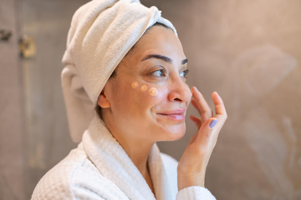 Mature woman applying makeup for eczema in mirror