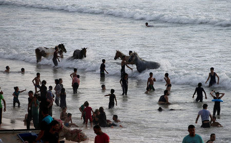 Palestinians wash horses as others swim to cool off in the Mediterranean Sea off the coast of the northern Gaza Strip July 13, 2018. REUTERS/Mohammed Salem