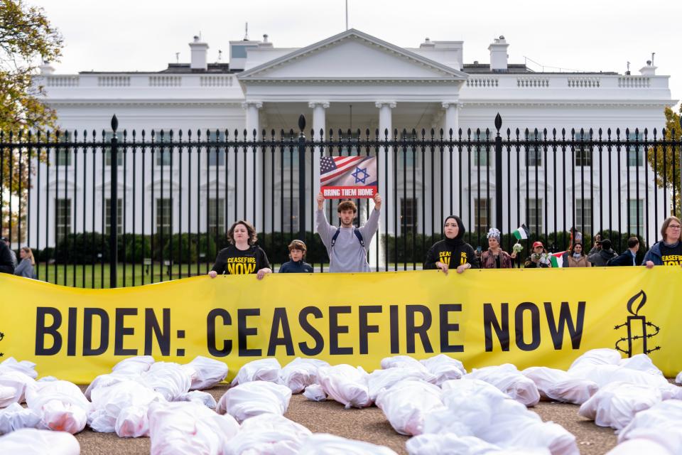 A man visiting from New Jersey holds up a poster in support of bringing Israeli hostages home behind a protest where a large banner that says "Biden: Ceasefire Now."