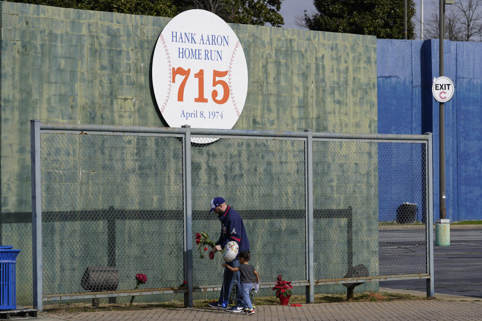 Les Motes and his two-year-old daughter Mahalia leave flowers, Friday, Jan. 22, 2021, in Atlanta, near the spot where a ball hit for a home run by Atlanta Braves' Hank Aaron cleared the wall to break Babe Ruth's career home run record in 1974. Aaron, who endured racist threats with stoic dignity during his pursuit of Babe Ruth but went on to break the career home run record in the pre-steroids era, died peacefully in his sleep early Friday. He was 86. (AP Photo/John Bazemore)