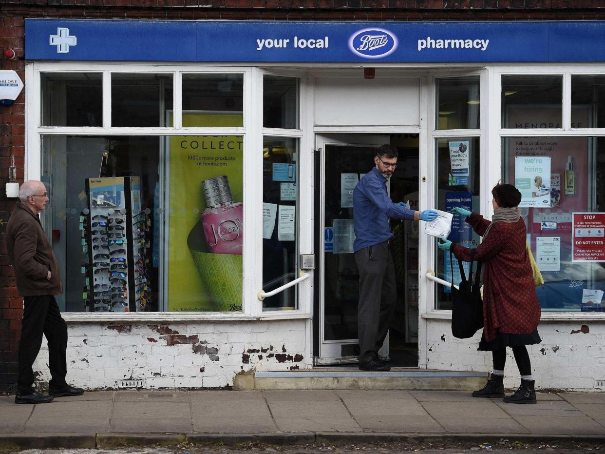 An employee hands a customer her prescription medicines as she adheres to social distancing guidelines outside a Boots pharmacy store in York: AFP via Getty Images