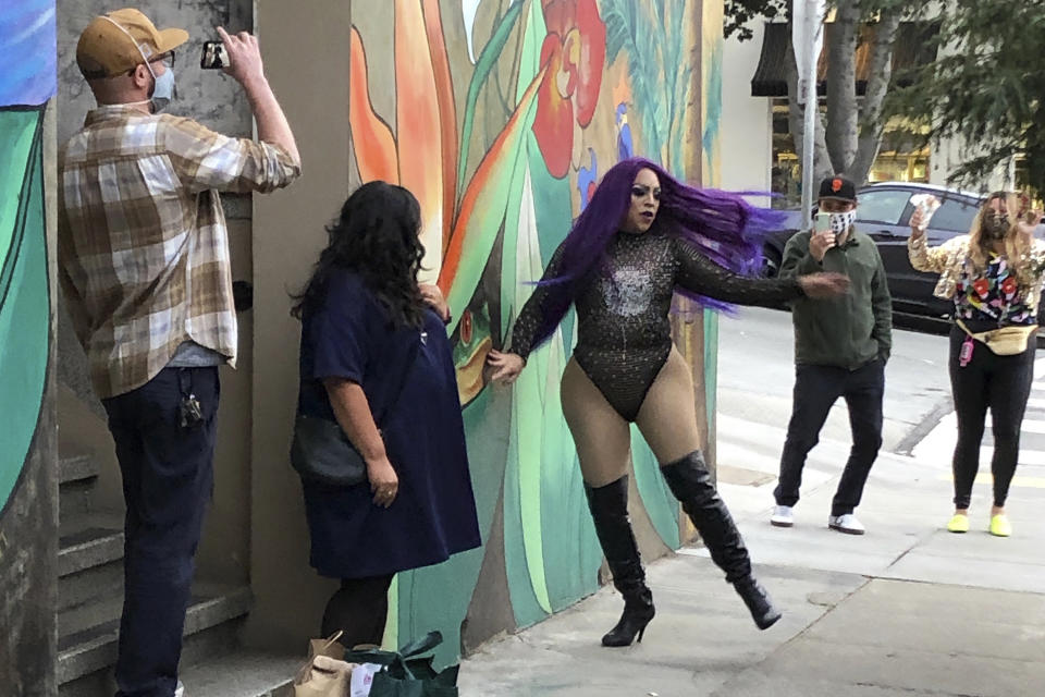 This Friday, Aug. 28, 2020, photo shows Amoura Teese, center, performing on a sidewalk for customers in San Francisco. A San Francisco drag show night club has taken the show on the road after having to close its doors due to the coronavirus pandemic. Oasis' "Meals on Heals" is dispatching drag queens to deliver food, custom cocktails and socially-distant lip synch performances. (AP Photo/Haven Daley)