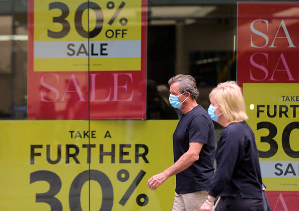 People wearing masks walk past sales sign at Pitt Street Mall in Sydney.