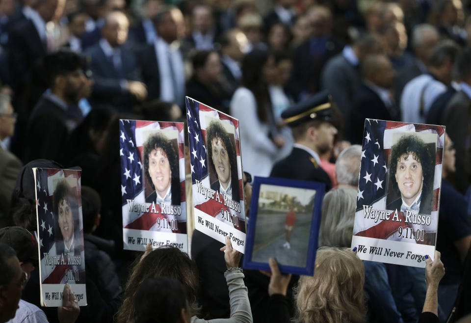 FILE - In this Sept. 11, 2017, file photo, people hold up signs with the names and pictures of victims of the 9/11 terrorist attacks during a ceremony at ground zero in New York. The coronavirus pandemic has reshaped how the U.S. is observing the anniversary of 9/11. The terror attacks' 19th anniversary will be marked Friday, Sept. 11, 2020, by dueling ceremonies at the Sept. 11 memorial plaza and a corner nearby in New York. (AP Photo/Seth Wenig, File)