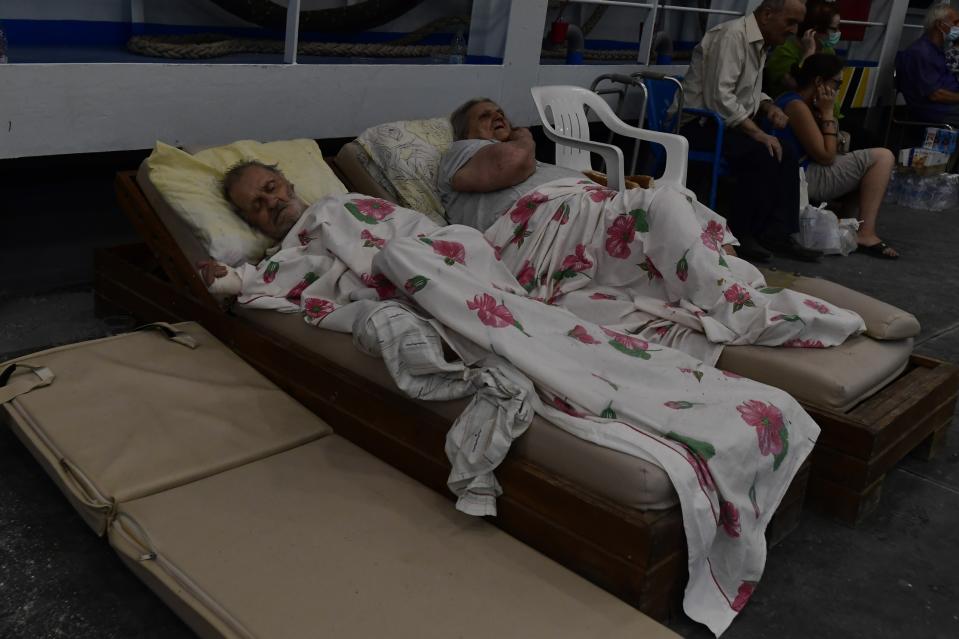 A man sleeps as a woman speaks on her cellphone in a docked ferry during a wildfire at Pefki village on Evia island, about 189 kilometers (118 miles) north of Athens, Greece, Sunday, Aug. 8, 2021. The fire in Evia, Greece's second-largest island, began Aug. 3 and has cut across the popular summer destination from coast to coast as it burned out of control. (AP Photo/Michael Varaklas)