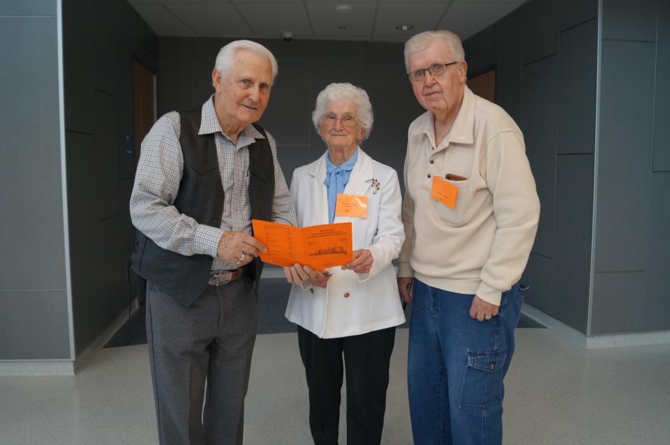 Richard Dilgard (left), president of alumni, and Anna Mae (Glass) Beecher, member of oldest class, look at program with Bill Glass (right), alumni secretary, and brother of Anna Mae.
