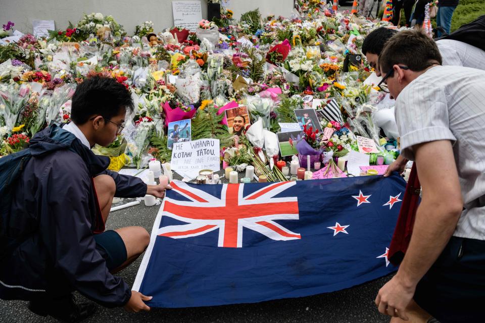 Students display the New Zealand national flag next to flowers during a vigil in Christchurch on March 18, 2019, three days after a shooting incident at two mosques in the city that claimed the lives of 50 Muslim worshippers.