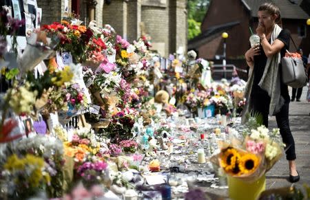 A woman looks at flowers, tributes and messages left for the victims of the fire at the Grenfell apartment tower in North Kensington, London, Britain, June 23, 2017. REUTERS/Hannah McKay