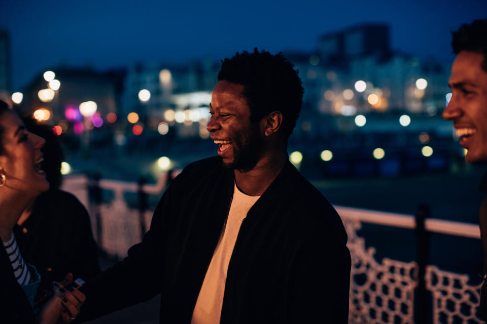 Three friends laughing with each other, outside on a balcony at night