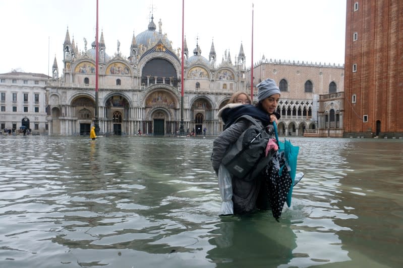 A woman carrying a child on her back wades in the flooded St. Mark's Square in Venice, Italy