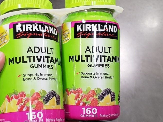 Hand holding a two-pack of green containers of kirkland multivitamins