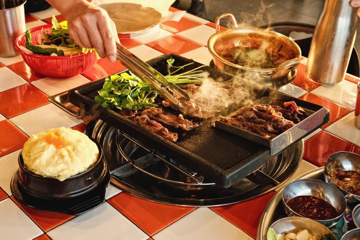 A hand holding a set of tongs cooks brisket at K-Team BBQ in Koreatown.