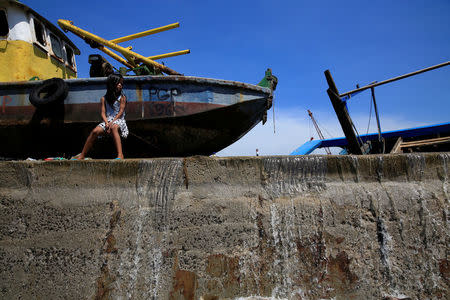 A girl sits next to a boat as sea water overflows on top of a concrete sea wall at the Muara Baru fishing port in Jakarta, Indonesia, December 6, 2017. REUTERS/Beawiharta