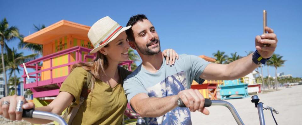 Young couple riding bikes in Miami beach, taking selfie pictures