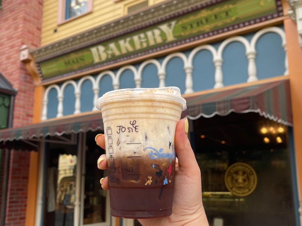 hand holding starbucks cup in front of main street bakery at magic kingdom in disney world