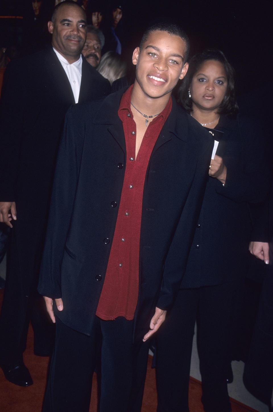 Smiling Robert in a long jacket, open shirt, and loose pants