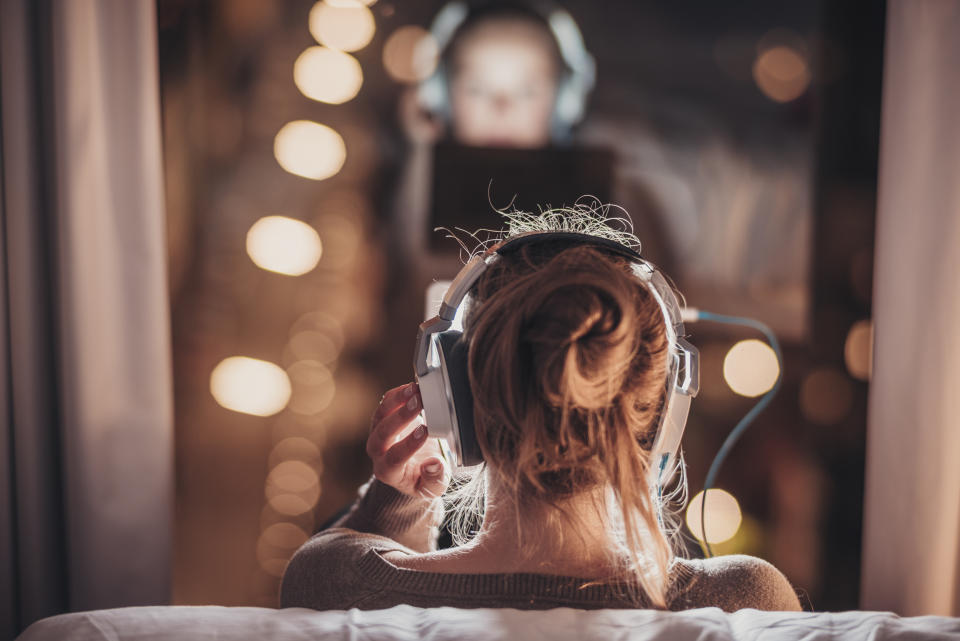 Woman using tablet pc in evening wearing big headphones, sitting in front of a big window.