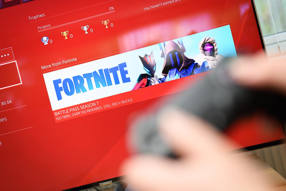 A person holds a controller in front of a screen with a Fortnite image on it 