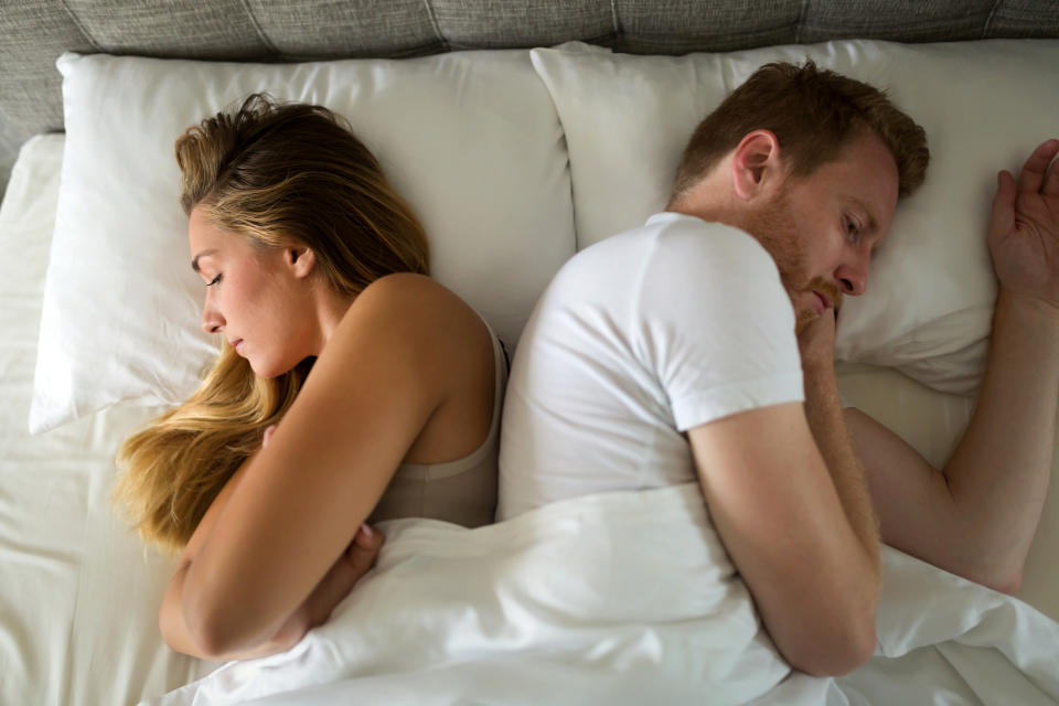 A couple lie in bed back-to-back, appearing upset or distant