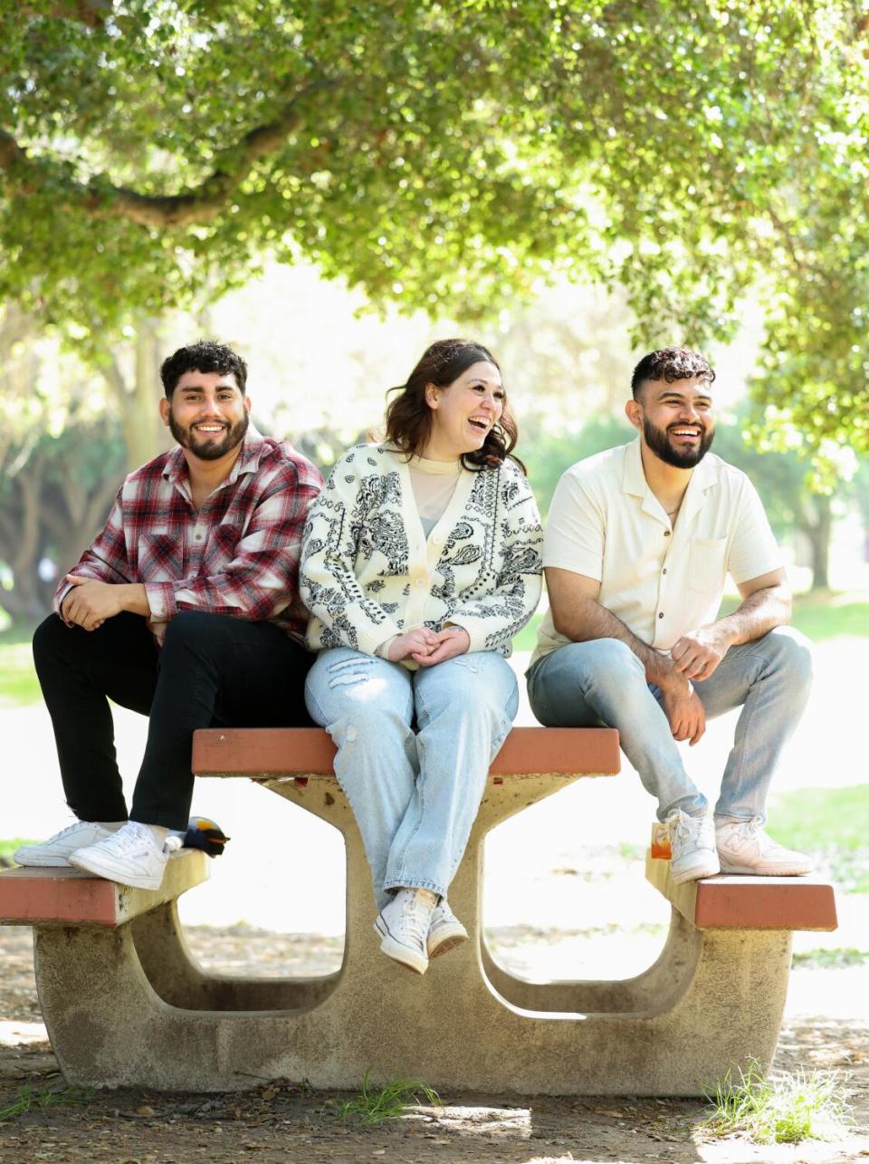 A woman sits between two men at the end of a picnic table, grinning.