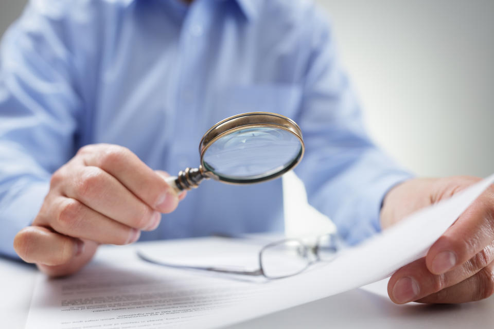 Man looking at a report with a magnifying glass.