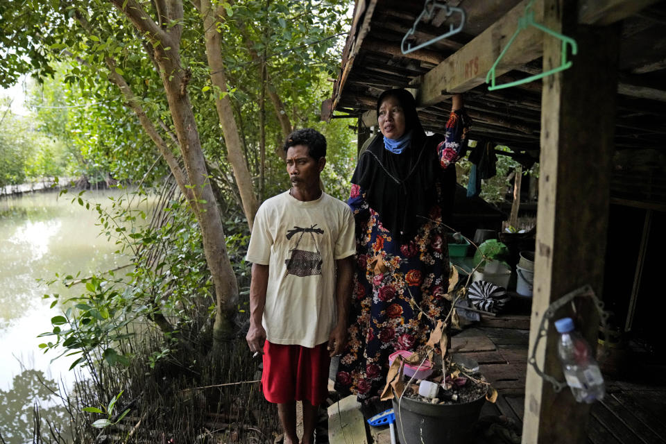 Asiyah, right, and her husband Aslori pose for a photo outside their old house they abandoned due to flooding in Mondoliko, Central Java, Indonesia, Monday, Sept. 5, 2022. They eventually moved to drier land, becoming climate migrants as many of their neighbors had before them. (AP Photo/Dita Alangkara)