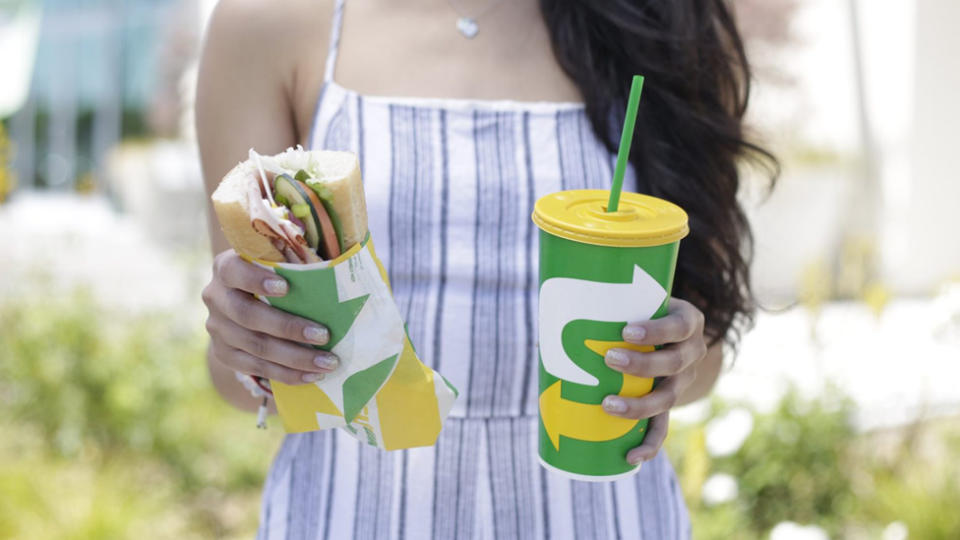 A woman holding a Subway sandwich and a Subway drink.