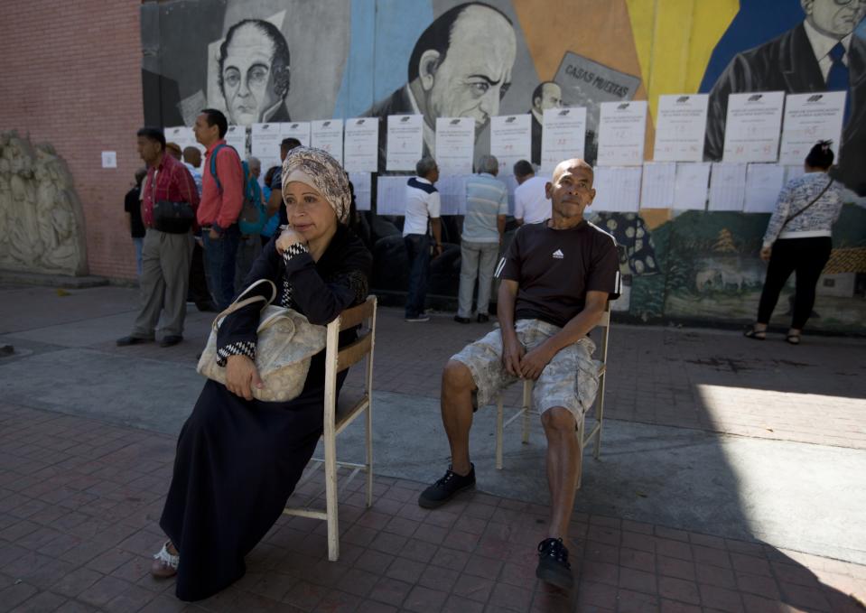 Dos electores aguardan antes de depositar su voto mientras otros examinan listas para ver dónde deben votar durante los comicios locales en Caracas, Venezuela, el domingo 9 de diciembre de 2018. (AP Foto/Fernando Llano)