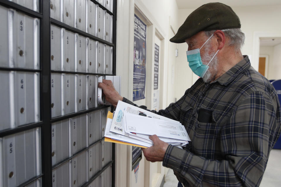 In this Wednesday, May 6, 2020 photo, Vaino Kola picks up his mail at the post office on Deer Isle, Maine. From coastal Maine to Philadelphia's close-knit neighborhoods, many residents call the postal service essential to their communities. (AP Photo/Robert F. Bukaty)