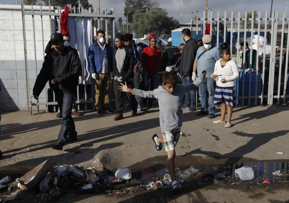 A boy leaps over a garbage-choked puddle as migrants walk out of an overflowing sports complex where more than 5,000 Central Americans are sheltering in Tijuana, Mexico, Wednesday, Nov. 28, 2018. As Mexico wrestles with what to do with the thousands of people camped out in the border city of Tijuana, President-elect Andres Manuel Lopez Obrador's government signaled Tuesday that it would be willing to house the migrants on Mexican soil while they apply for asylum in the United States, a key demand of U.S. President Donald Trump. (AP Photo/Rebecca Blackwell)