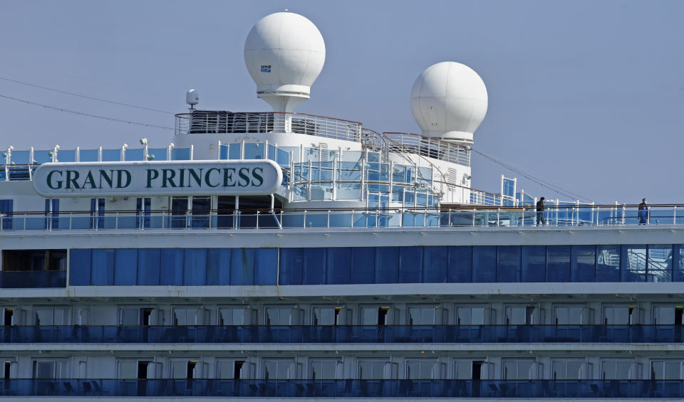 Two men wearing face masks stroll on the sun deck of the Grand Princess cruise ship while docked at the Port of Oakland Friday, March 13, 2020, in Oakland, Calif. The cruise ship was nearing the end of a tedious, days-long process of removing 2,000 passengers after more than 20 people on board had been diagnosed with the coronavirus. (AP Photo/Ben Margot)