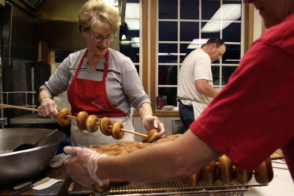 Spudnut owner Val Driver, left, and Barb Welch thread raised doughnuts onto dowels for glazing while Kevin Russell prepares cinnamon rolls and maple bars for frying.