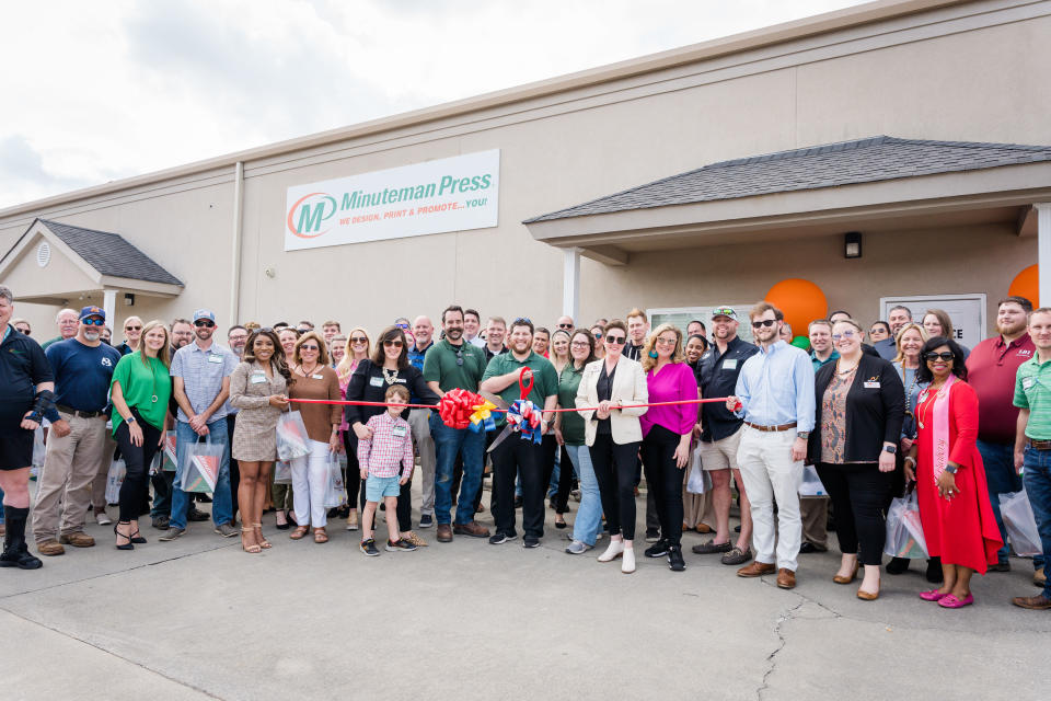 Minuteman Press, Macon, GA grand opening and ribbon-cutting ceremony at 4341 Interstate DR, Suite B, Macon GA 31210. Richie Moore (center, with scissors) is pictured alongside his wife Elle Moore as well as colleagues, friends, and community members.