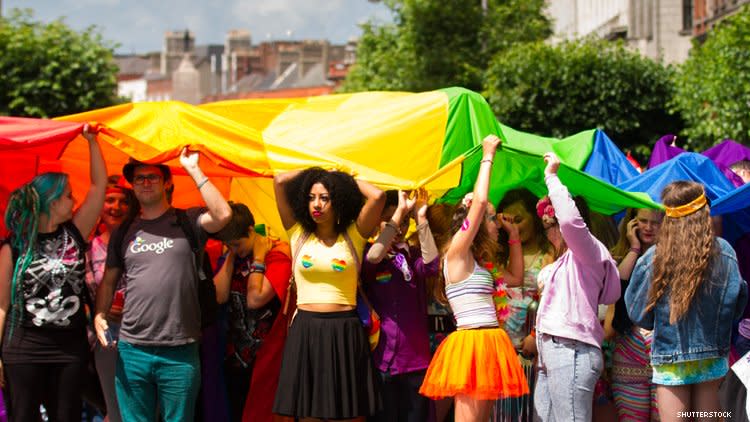 Group of LGBTQ people hold aloft a giant rainbow flag