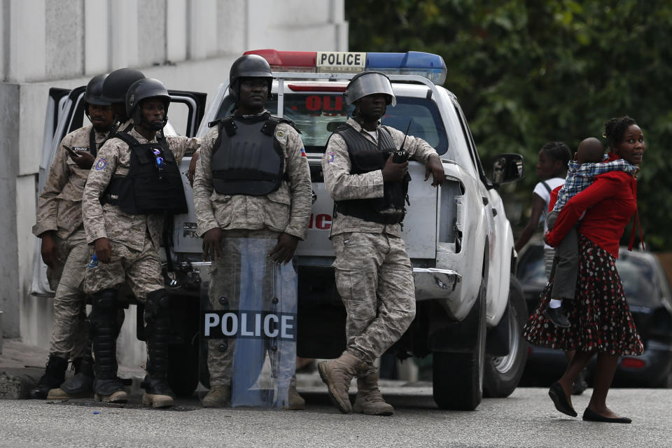 A woman carries a child past police standing guard during a protest led by the art community demanding the resignation of Haitian President Jovenel Moïse, in Petion-Ville, Port-au-Prince, Haiti, Sunday, Oct. 13, 2019.Thousands of Haitians joined a largely peaceful protest called by the art community Sunday to demand that Moïse step down, increasing pressure on the embattled leader after nearly a month of marches that have shuttered schools and businesses.(AP Photo/Rebecca Blackwell)