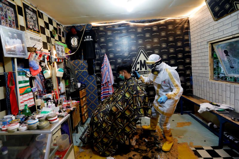 Herman Maulanasyah, a 40-year-old hair stylist, gives a haircut to a customer at his barbershop, while wearing a handmade protective suit in a tribute to the country's medical workers tackling the coronavirus disease (COVID-19) in Bogor