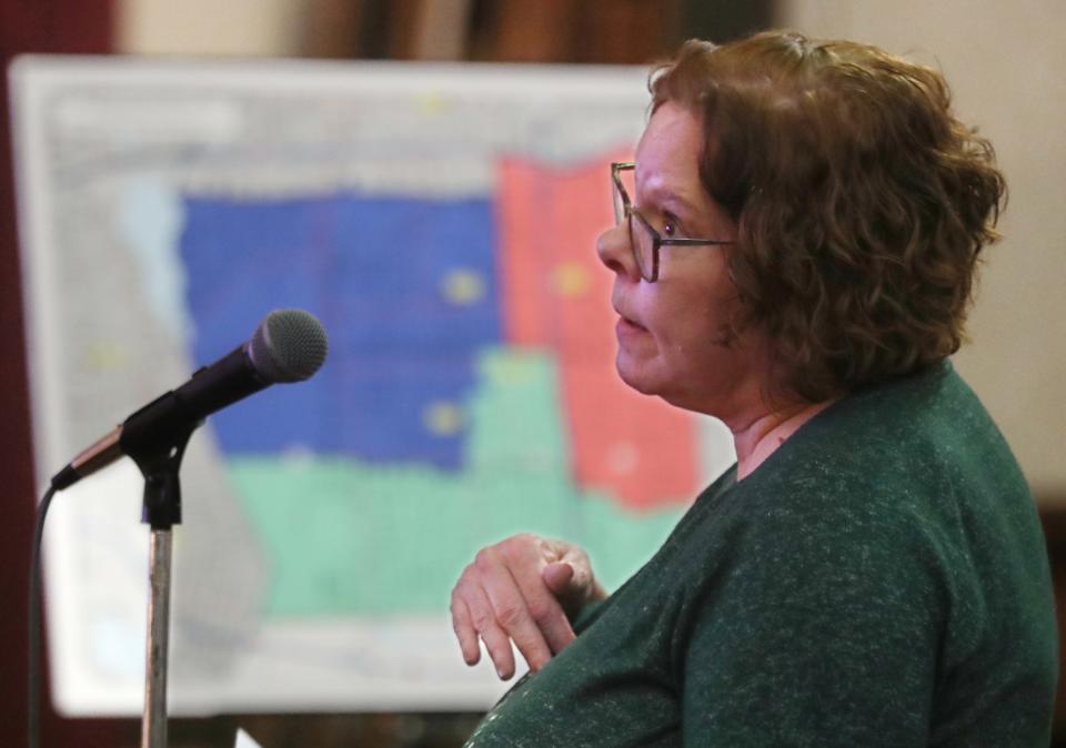 Kim Stimler, a Firestone Park resident, asks a question during a community meeting Monday about a proposed Akron Public Schools' redistricting plan. A draft option of the school cluster map is in the background.