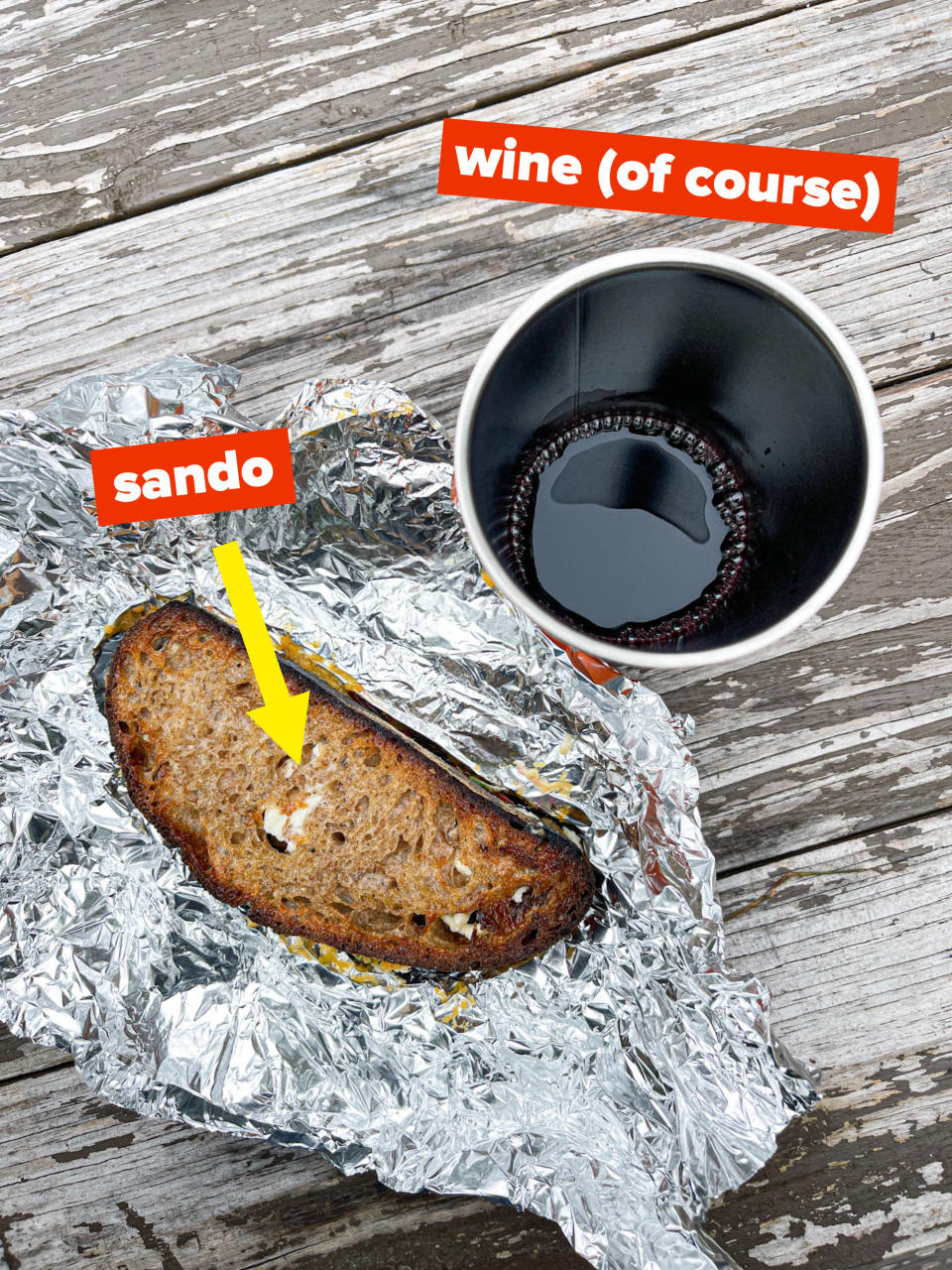 Sandwich wrapped in foil, with a cup of wine on a picnic table