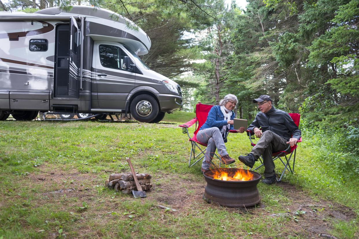 couple using digital tablet near campfire with RV parked in the background