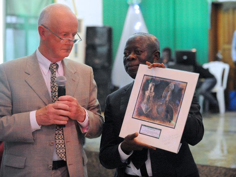 Edo State Governor Adams Oshiomhole (R) holds a catalogue of the Benin bronze artefacts returned by retired hospital consultant Mark Walker (L) during a ceremony in Benin City, Nigeria, on June 20, 2014