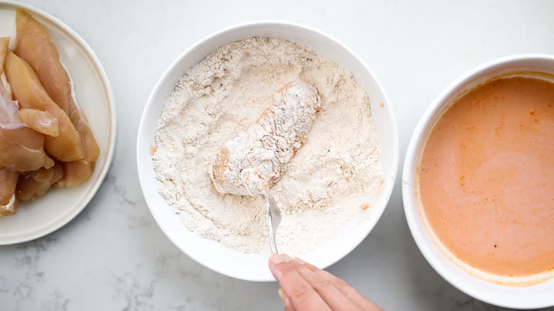 hand coating chicken in flour