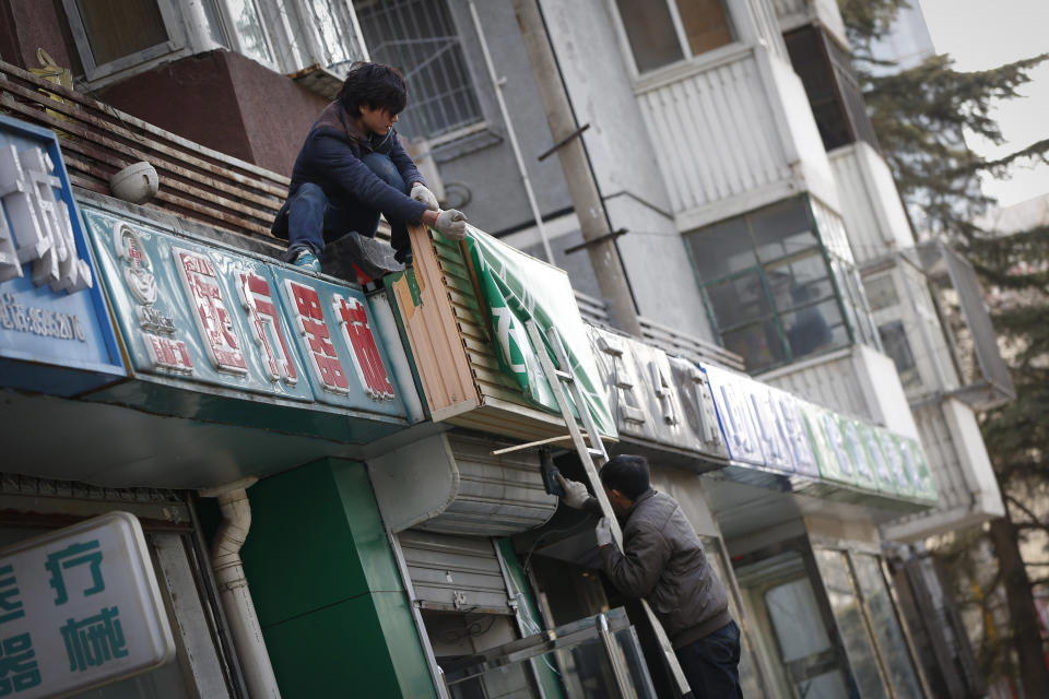 Worker changing a business signboard in downtown Beijing, China, Friday, March 7, 2014. China today expressed confidence over achieving its GDP target of 7.5 per cent this year, citing the expected recovery of the world economy and strong fundamentals of emerging markets. (AP Photo/Vincent Thian)