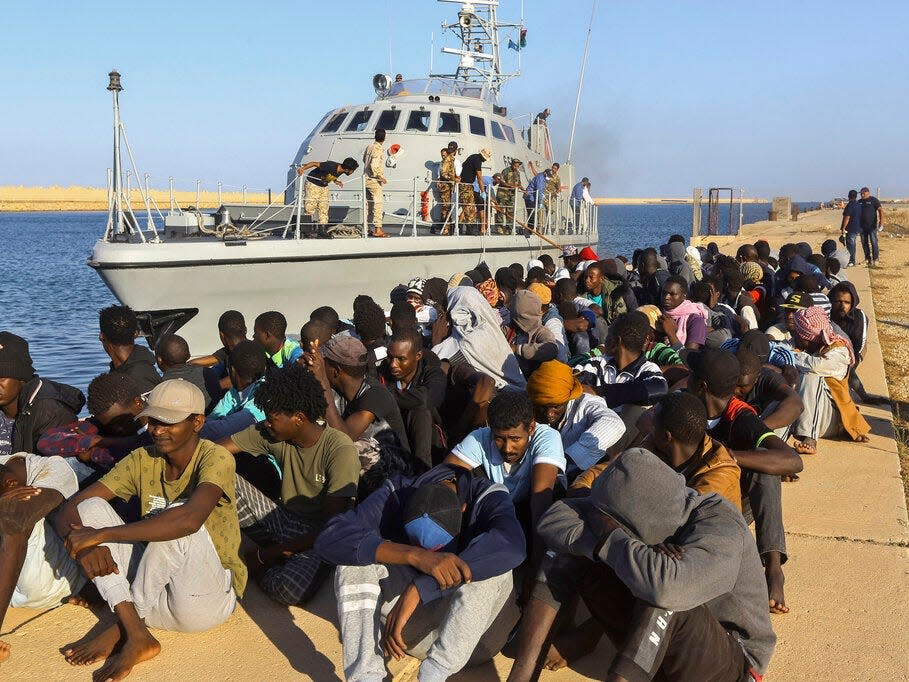 In this Tuesday, Oct. 1, 2019 file photo, rescued migrants are seated next to a coast guard boat in the city of Khoms, Libya, around 120 kilometers (75 miles) east of Tripoli.