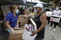 Salvation Army worker Brenda Gonzalez, of Saugus, Mass., left, distributes food to an unidentified man while others impacted by the coronavirus wait in line at a Salvation Army center, Tuesday, June 30, 2020, in Chelsea, Mass. (AP Photo/Steven Senne)