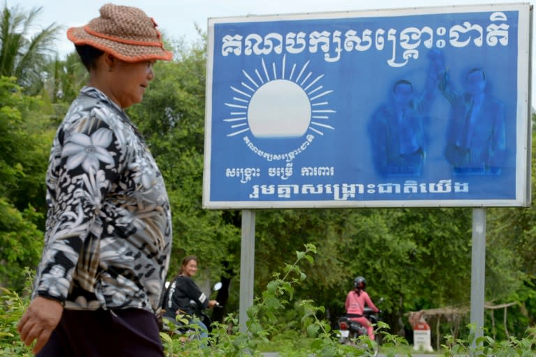 This picture taken on August 5, 2017 shows a woman walking past a billboard for the Cambodia National Rescue Party (CNRP) with covered up images of leader Kem Sokha (2nd R) and former leader Sam Rainsy (R), in a village in Pursat province