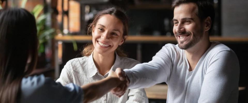 Happy smiling millennial couple get acquainted with female real estate agent meeting together in cafe.