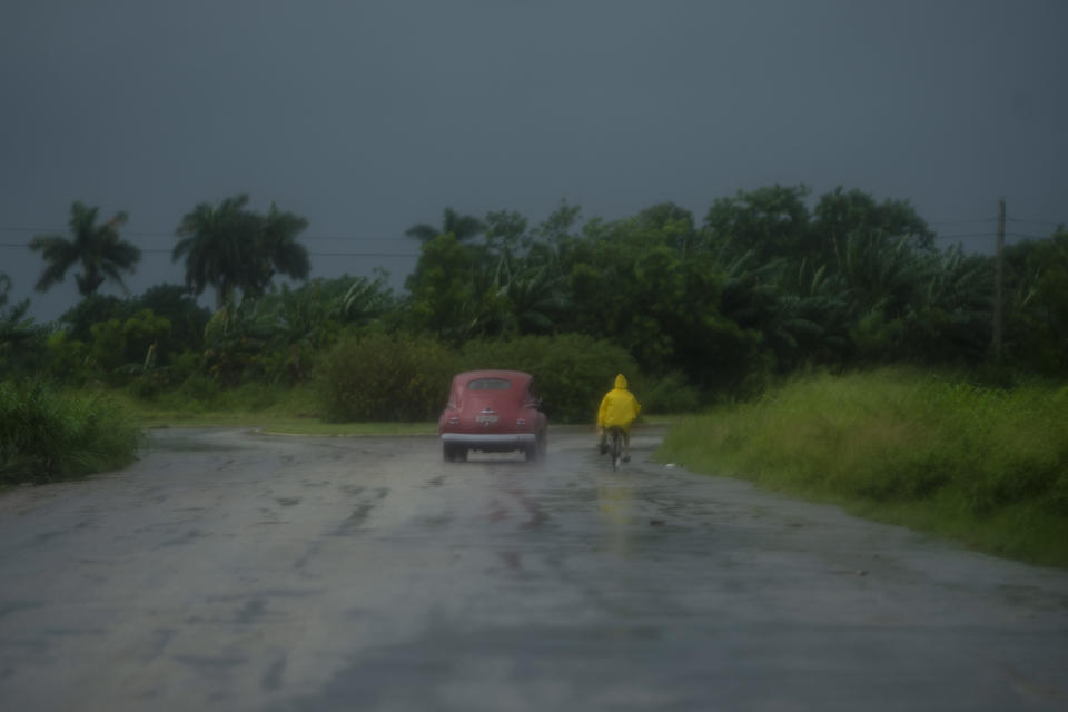 A man rides a bicycle alongside a car in rain caused by Hurricane Ida, in Guanimar, Artemisa province, Cuba, Saturday Aug. 28, 2021. (AP Photo/Ramon Espinosa)